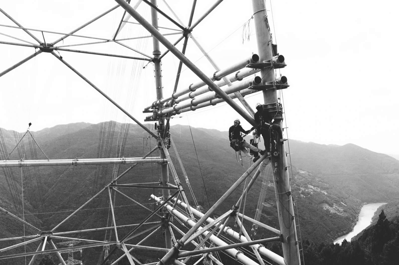 山岳地帯の送電線鉄塔で作業する 2 名の職人